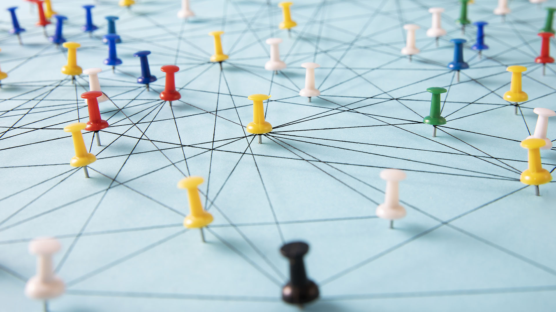 Peering automation at Facebook - An arrangement of colorful pins linked together with string on a pale blue background suggesting a network of connections.